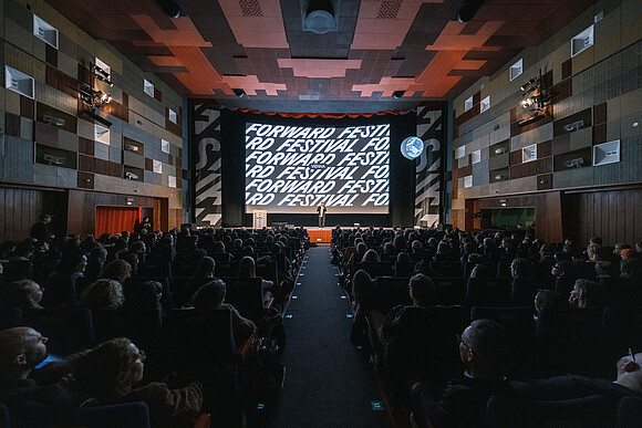 Cinema screen of the Gartenbau Kino with Forward Festival inscription and full cinema hall