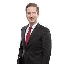 Felix Schneider standing, wearing a dark jacket and a red tie