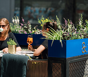 Two people are sitting in the outdoor dining area with a drink