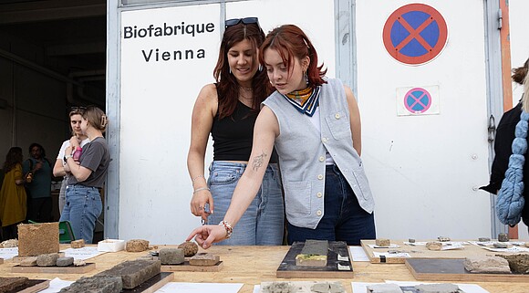 Two people are looking at materials in front of the Biofabrique Vienna Hall.