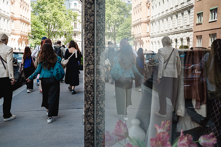 A group of people seen from behind walking on the sidewalk. Reflectiong in the shopping window.