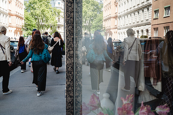 A group of people seen from behind walking on the sidewalk. Reflectiong in the shopping window.