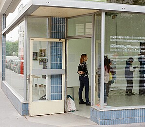 People in an art space, a shopfront with a glass façade