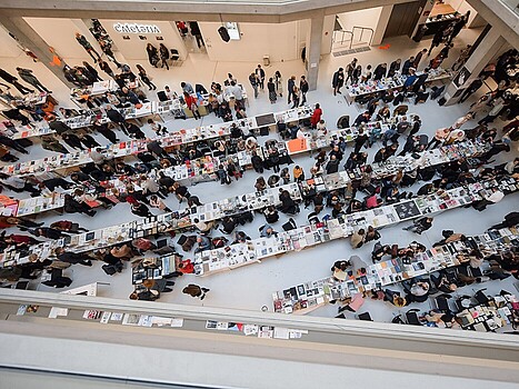 Blick von oben auf eine große Buchmesse und lesende Menschen
