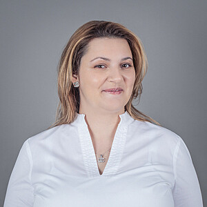 Porträt von Sanela Stepanovc, eine Frau in weißer Bluse mit schulterlangen, brünetten Haaren