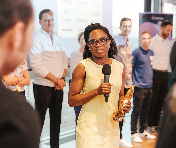 Woman in yellow dress speaking into a microphone to a group of people at a business event