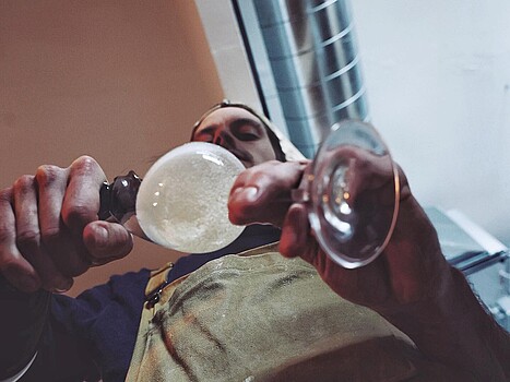 A Tho baker in an apron carefully pours a glass of wine, captured from an unusual perspective.