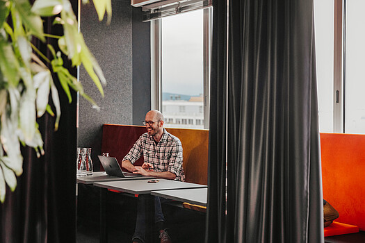 Mann im karierten Hemd sitzt an einem Tisch vor einem Laptop