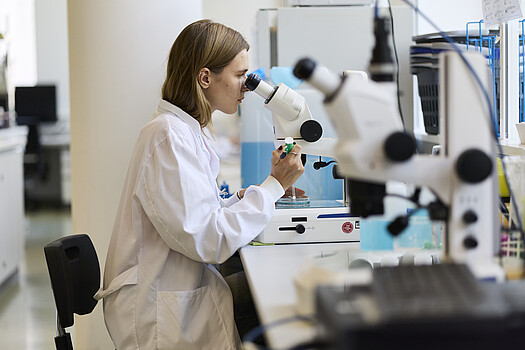 Eine Frau im Laborkittel schaut in ein Mikroskop in einem Labor.