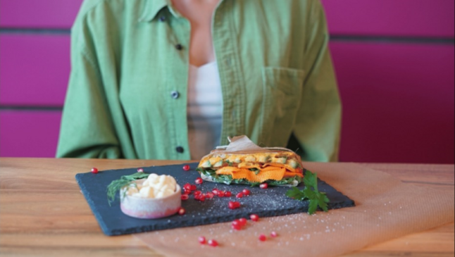 Revo Foods: Eine Frau in grünem Hemd sitzt an einem Tisch auf dem ein Lachsbagel liegt.